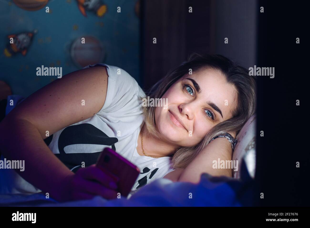 Junge Frau, die im Bett mit dem Telefon liegt und anschaut Die Kamera Stockfoto