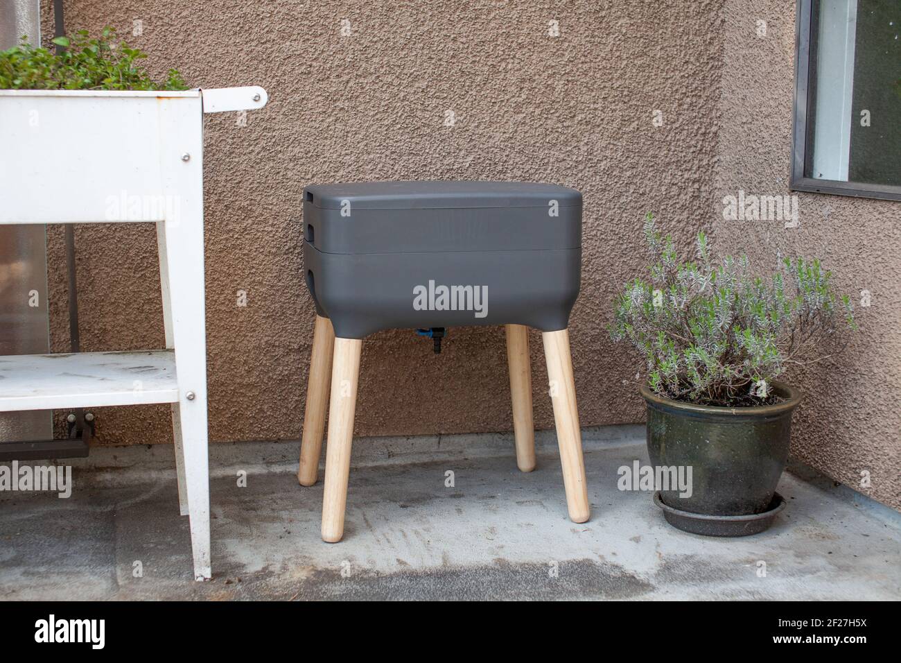 Ein Vermicomposting-System (Wurm Komposter) sitzt auf einem Apartment-Balkon mit anderen Gartenbepflanzungen. Würmer essen Lebensmittelreste und produzieren Wurmgussteile und Stockfoto