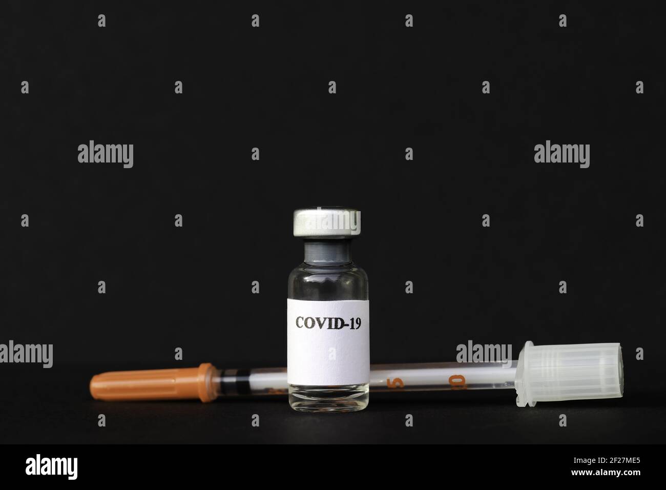 Eine Corona-Impfampulle und Spritze vor schwarzem Hintergrund Stockfoto