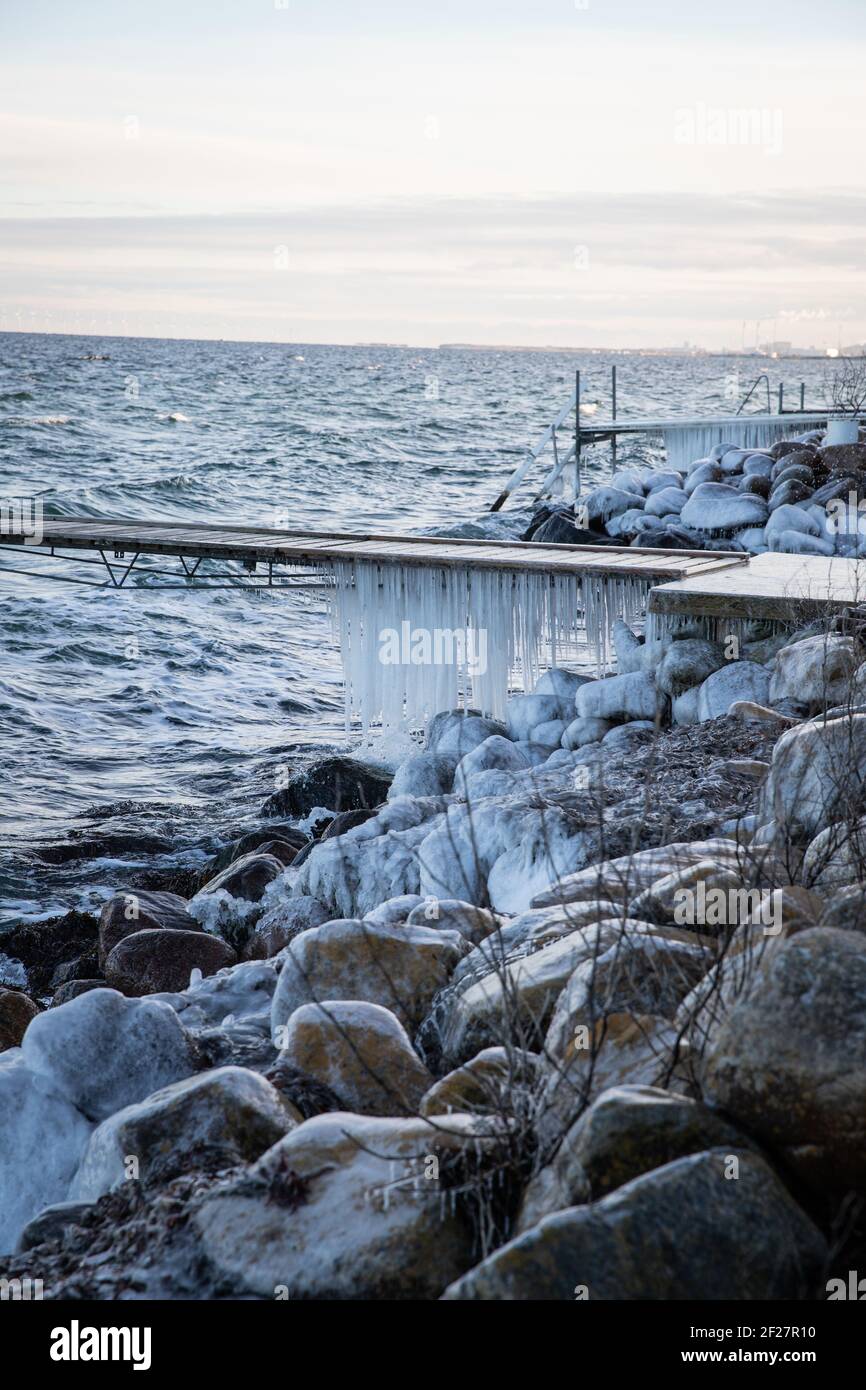 Eiszapfen hängen an einer gefrorenen Brücke an der Küste. Kalter Wintertag. Stockfoto