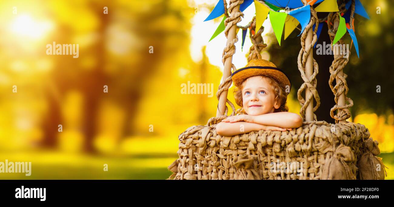 Kleiner hübscher Junge sitzt in einem Korb aus einem Ballon und Träume blicken in den Himmel. Stockfoto