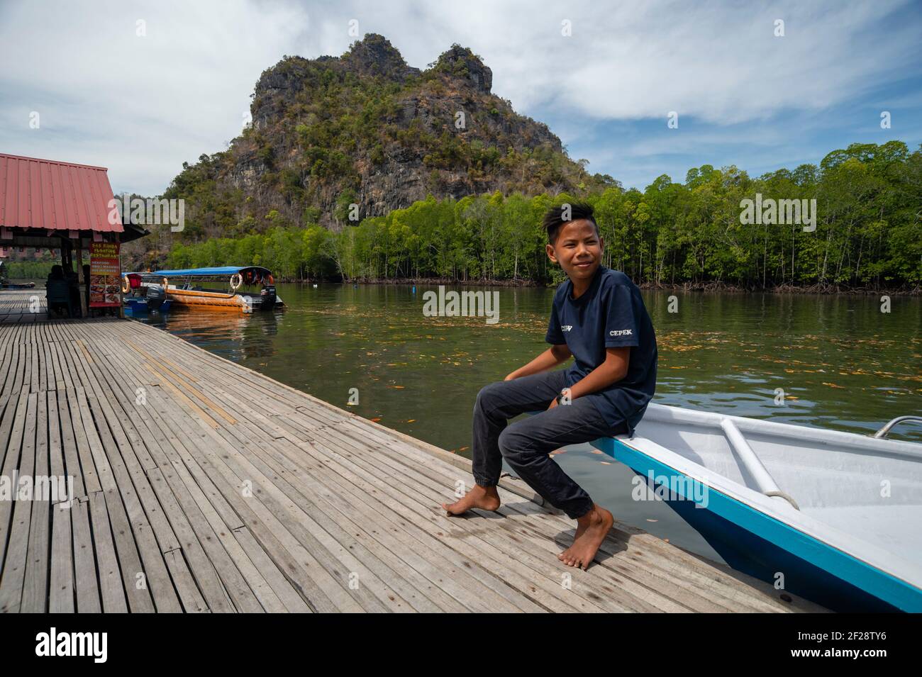 Kleiner Junge, der auf einem Boot auf einer schwimmenden Fischfarm sitzt. Stockfoto