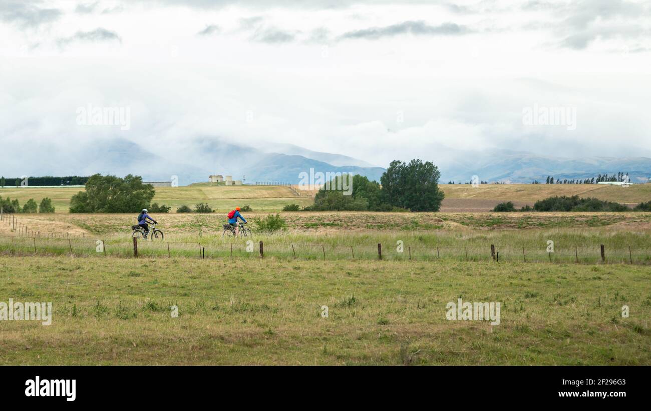 Zwei Radfahrer fahren den Otago Rail Trail mit Wolken bedeckt Die Berge des malerischen Central Otago Stockfoto