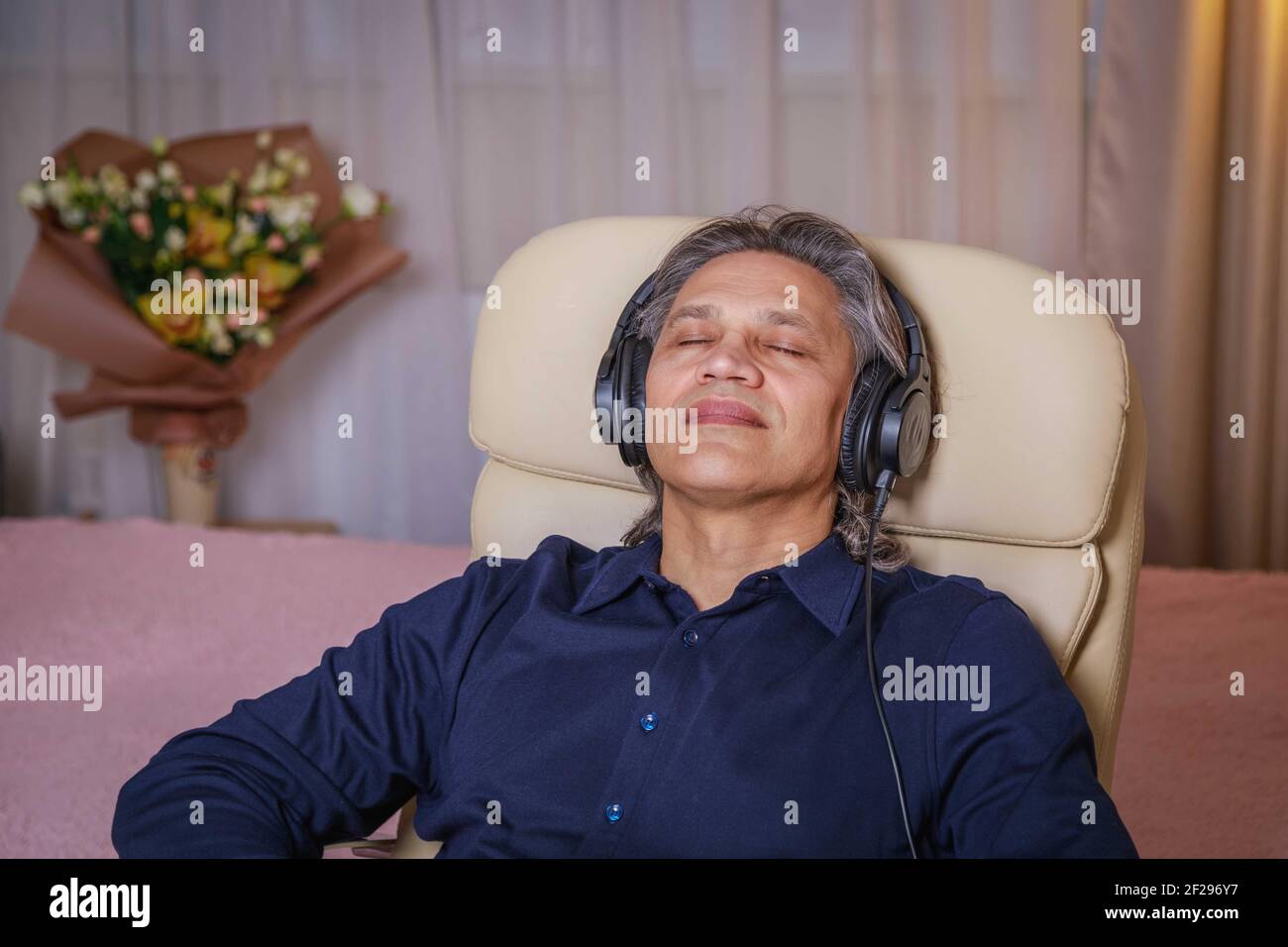 Der 50-jährige Mann hört zu Hause Musik auf Kopfhörern, sitzt auf einem Stuhl. Erholsame Freude. Stockfoto