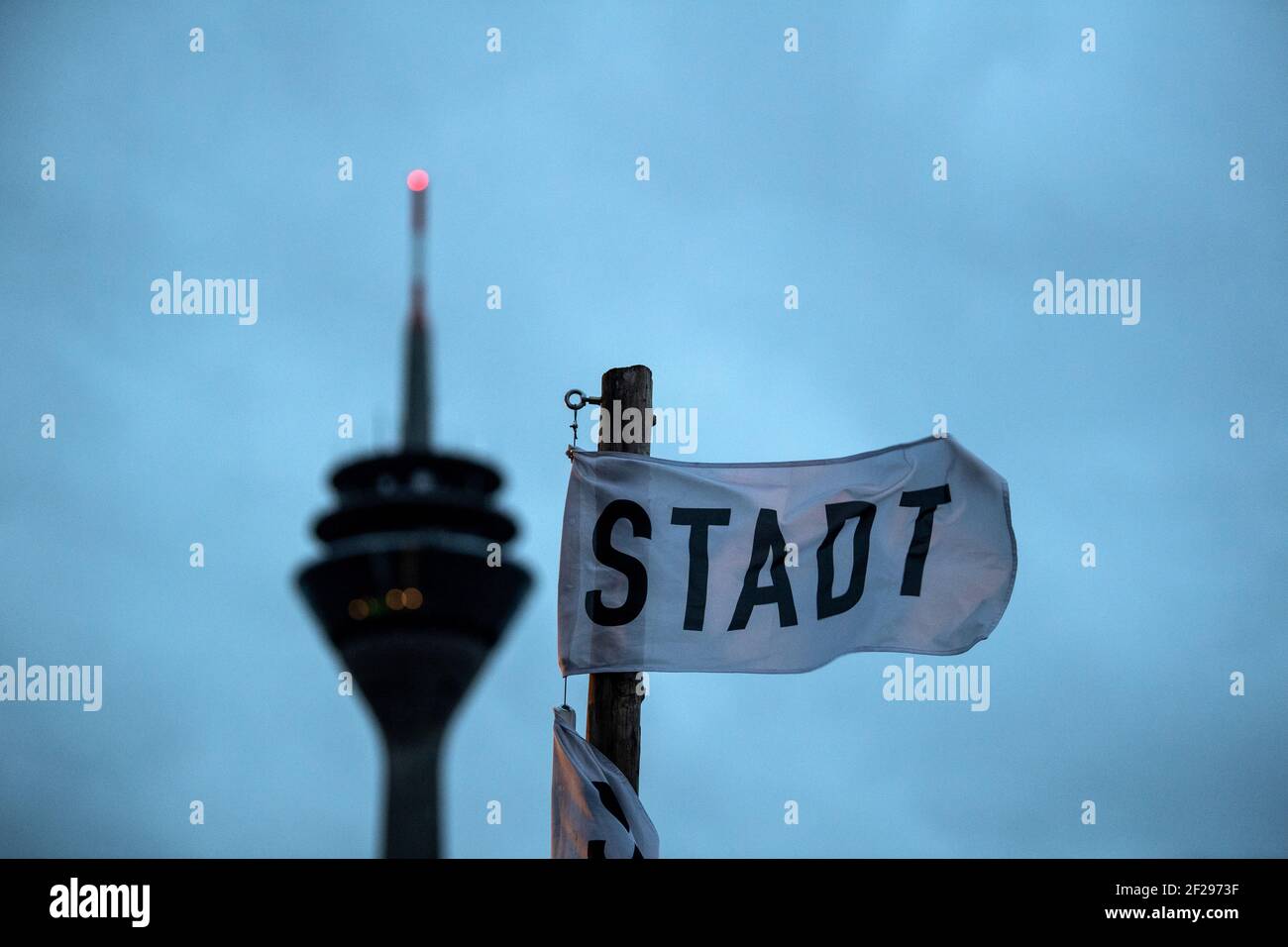 Düsseldorf, Deutschland. März 2021, 11th. Am frühen Morgen fliegt eine kleine Fahne mit der Aufschrift "Stadt" am Rheinufer, dahinter ist der Fernsehturm zu sehen. Der niedrige Klaus bringt in den nächsten Tagen stürmische Winde in Teilen Nordrhein-Westfalens. Das tief bringt aber für die Jahreszeit eher milde Luft nach Nordrhein-Westfalen. Quelle: Federico Gambarini/dpa/Alamy Live News Stockfoto