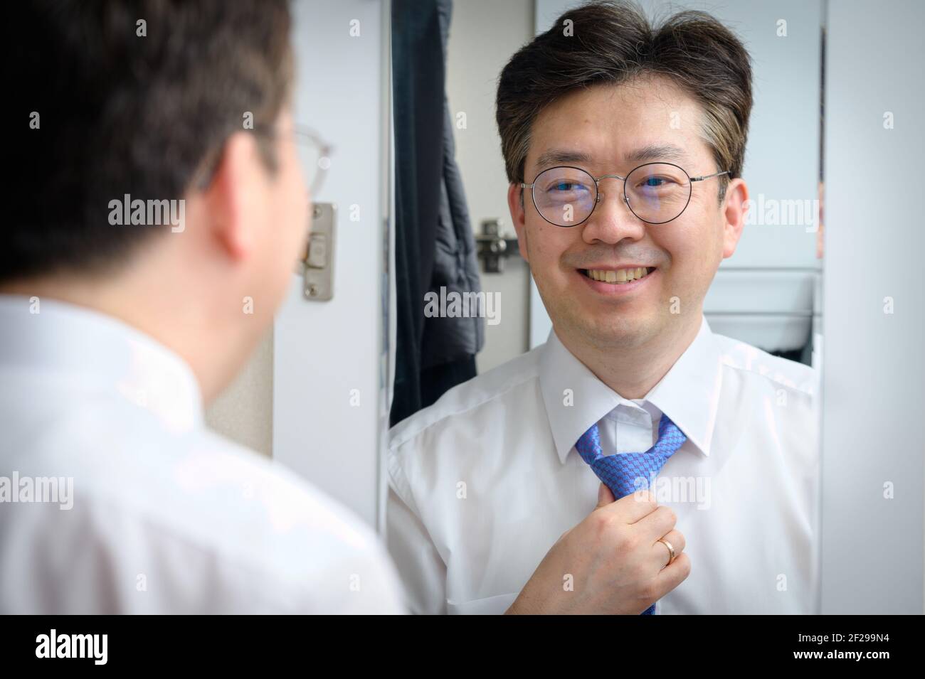 Ein asiatischer Geschäftsmann mittleren Alters lächelt, während er den Spiegel anschaut Am Morgen Stockfoto