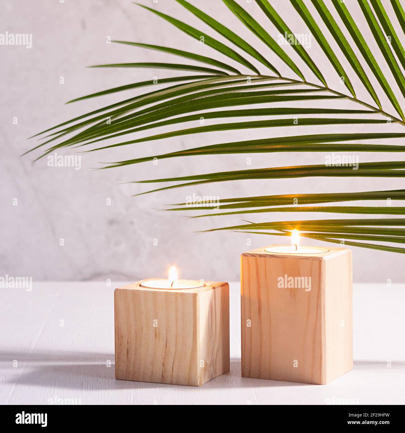 Wellness-Home-Dekor für Entspannung mit brennenden Kerzen und grünen Palmenblatt auf weißem Holztisch und Marmorwand, quadratisch. Stockfoto