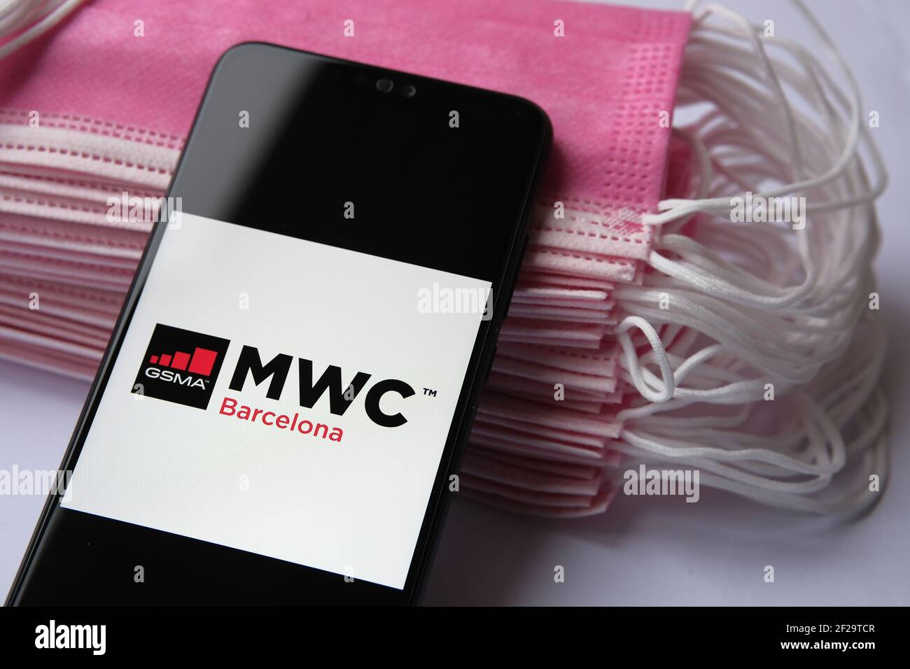 Mobile World Congress Barcelona Logo auf dem Bildschirm des Smartphones und Haufen von Gesichtsmasken auf dem Hintergrund gesehen. Konzept für Veranstaltung während COVID pandemi Stockfoto