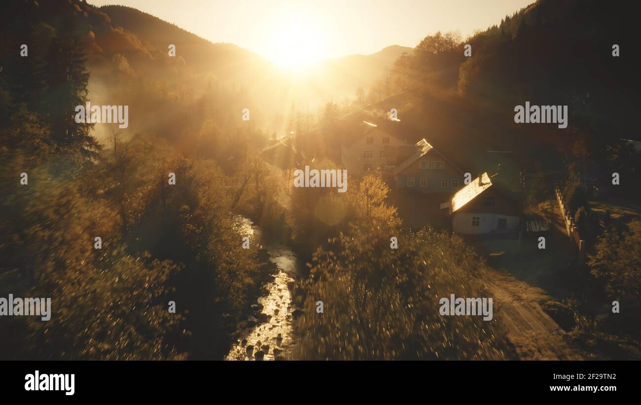 Sonnenuntergang über dem Bergdorf an der Kiefernwald-Antenne. Niemand Natur Landschaft. Herbst Laubbäume bei Abendnebel. Hütten auf dem Land Sonnenkämme. Reise zu den ländlichen Karpaten, Ukraine, Europa Stockfoto