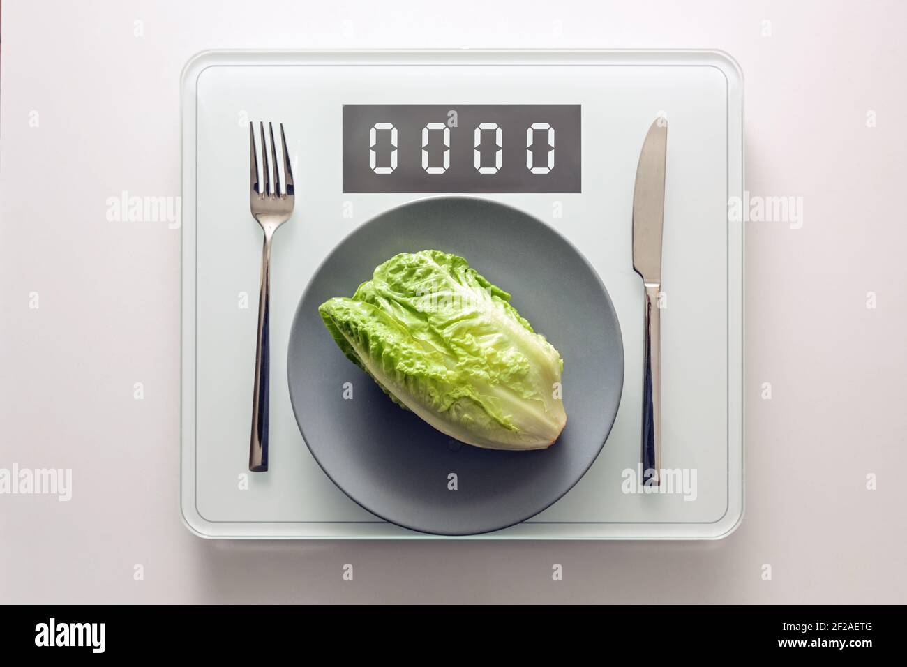 Frischer grüner Salat oder Baby cos auf einem grauen Teller und Besteck auf einer digitalen Waage, die Null, gesunde Ernährung und Gewicht verlieren Konzept, Kopierer Platz, Stockfoto