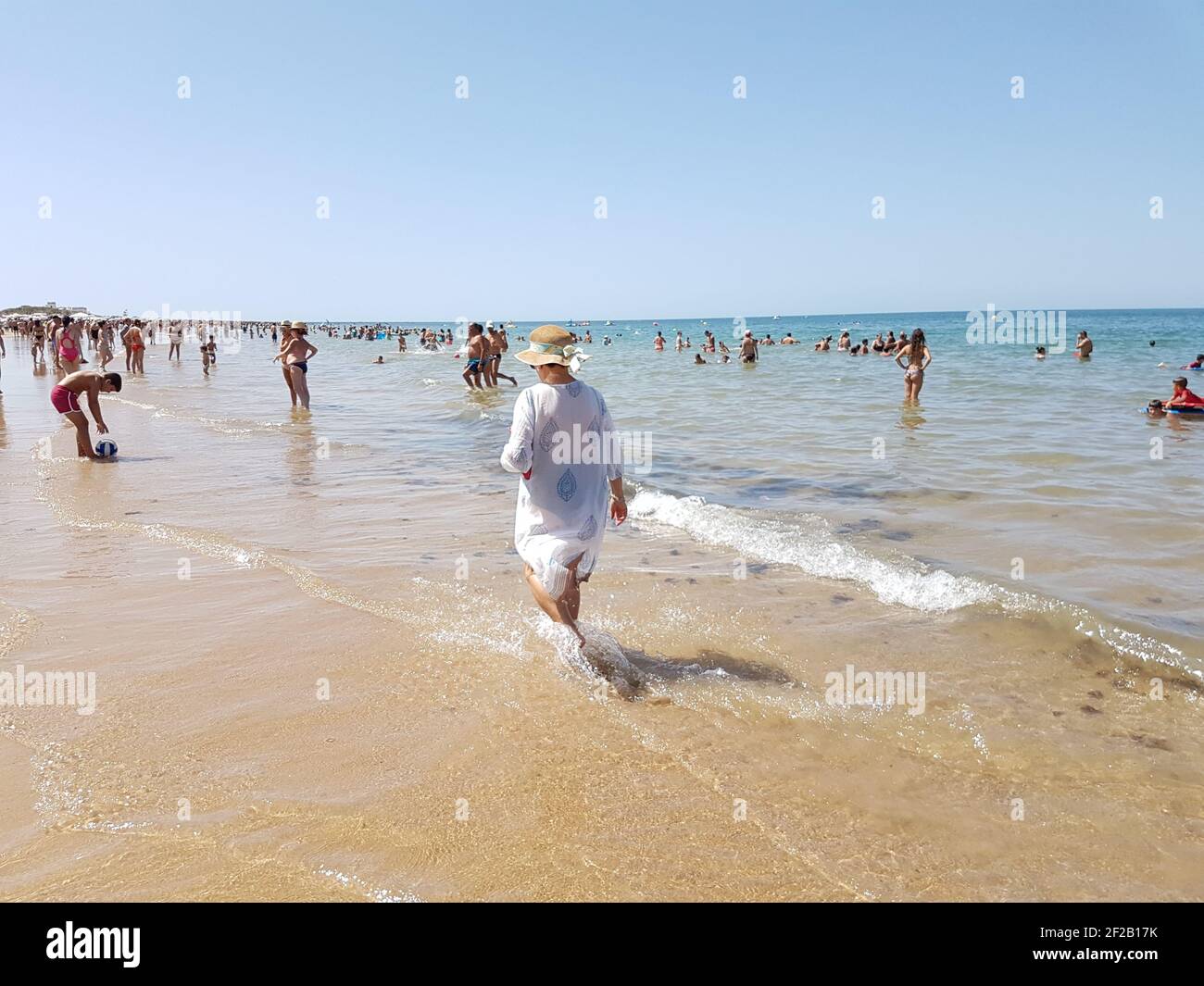 CHIPIONA, SPANIEN - 13. Aug 2017: Frau, die im Sommer unter den Menschen am Strand läuft Stockfoto