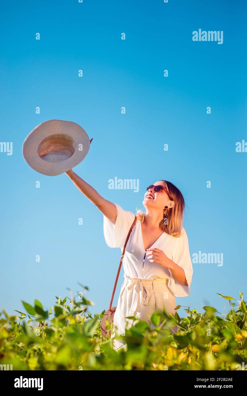 Fröhlich stilvolle junge Frau mit Hut in der Hand in Offenes Sommerfeld lächelnd Stockfoto