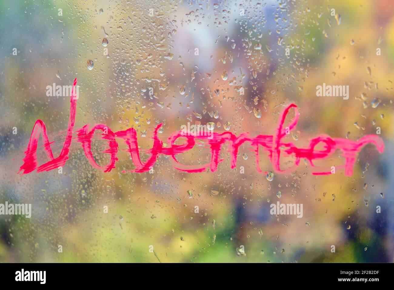 'November' steht auf der Fensterscheibe. Glas mit Regentropfen auf dem Herbstfenster Stockfoto