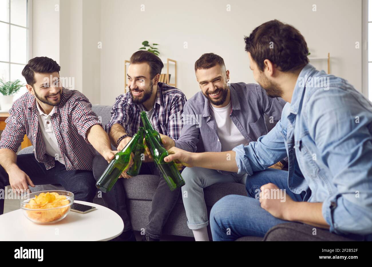 Gruppe von glücklichen jungen Männern auf der Couch sitzen und klirren Bierflaschen nach lustigen Toast Stockfoto