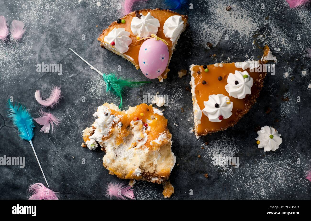 Blick in den Hochwinkel von einigen Stücken einer mona de pascua, einem Kuchen, der am Ostermontag in Spanien gegessen wurde, verziert mit einem rosa Ei und Federn in verschiedenen Farben Stockfoto