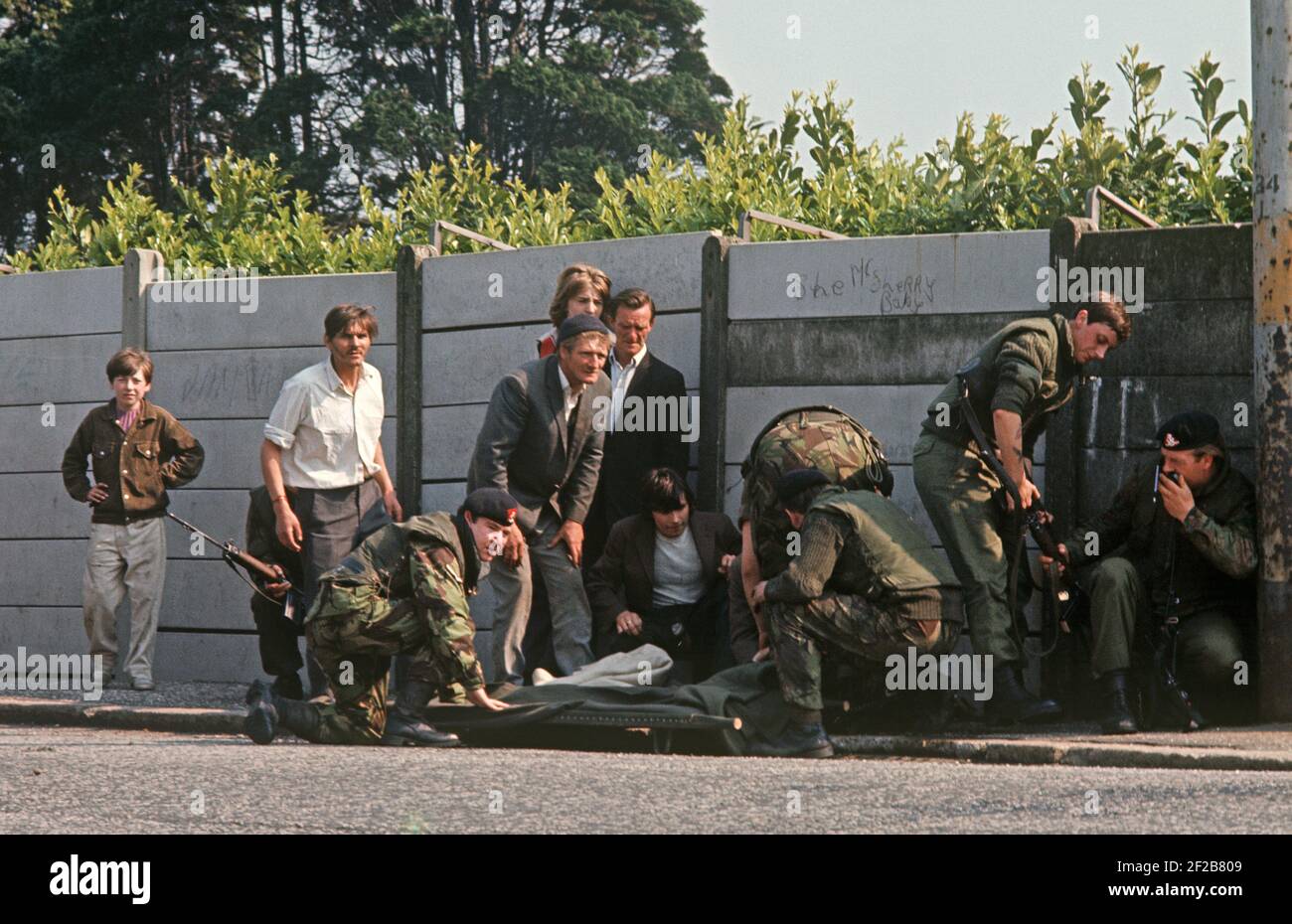 BELFAST, VEREINIGTES KÖNIGREICH - JUNI 1972. Soldaten der britischen Armee und Zivilisten, die während eines IRA-Scharfschützen-Angriffs, bei dem ein Schulmädchen verwundet wurde, Schutz bekamen, Ballymurphy, West-Belfast während der Unruhen, Nordirland, 1970er Jahre Stockfoto