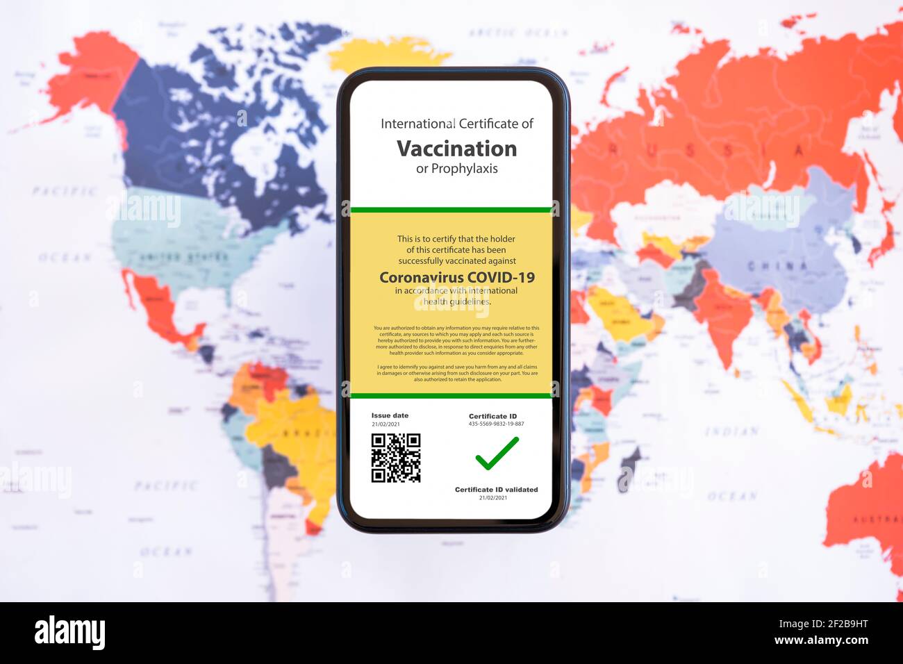 Flat Lay, ein Smartphone mit Impfpass gegen den Covid-19 ist auf einer verschwommenen Weltkarte angeordnet. Stockfoto