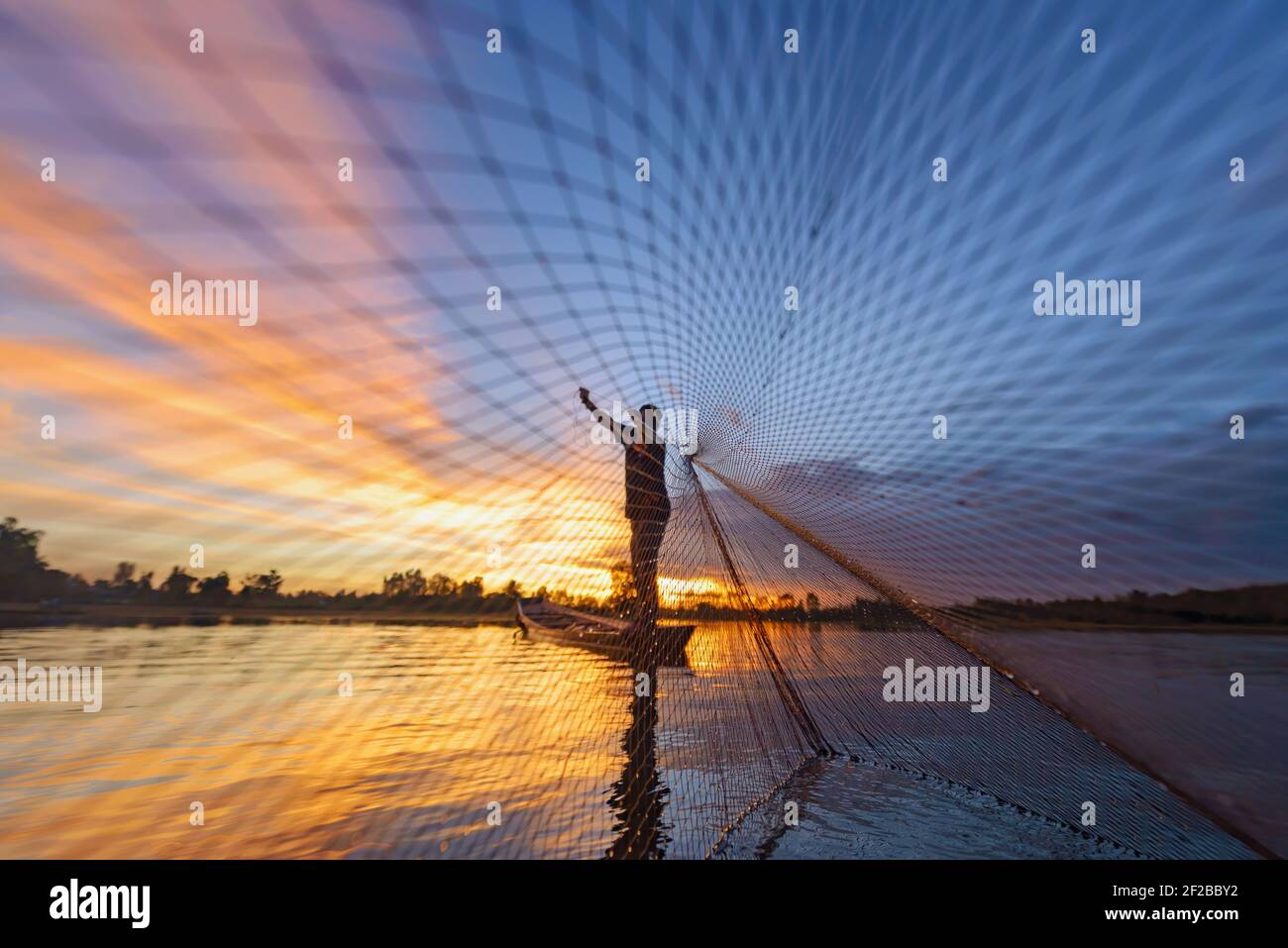 Silhouette eines Fischers, der in einem Boot steht und bei Sonnenuntergang ein Fischernetz wirft, Thailand Stockfoto