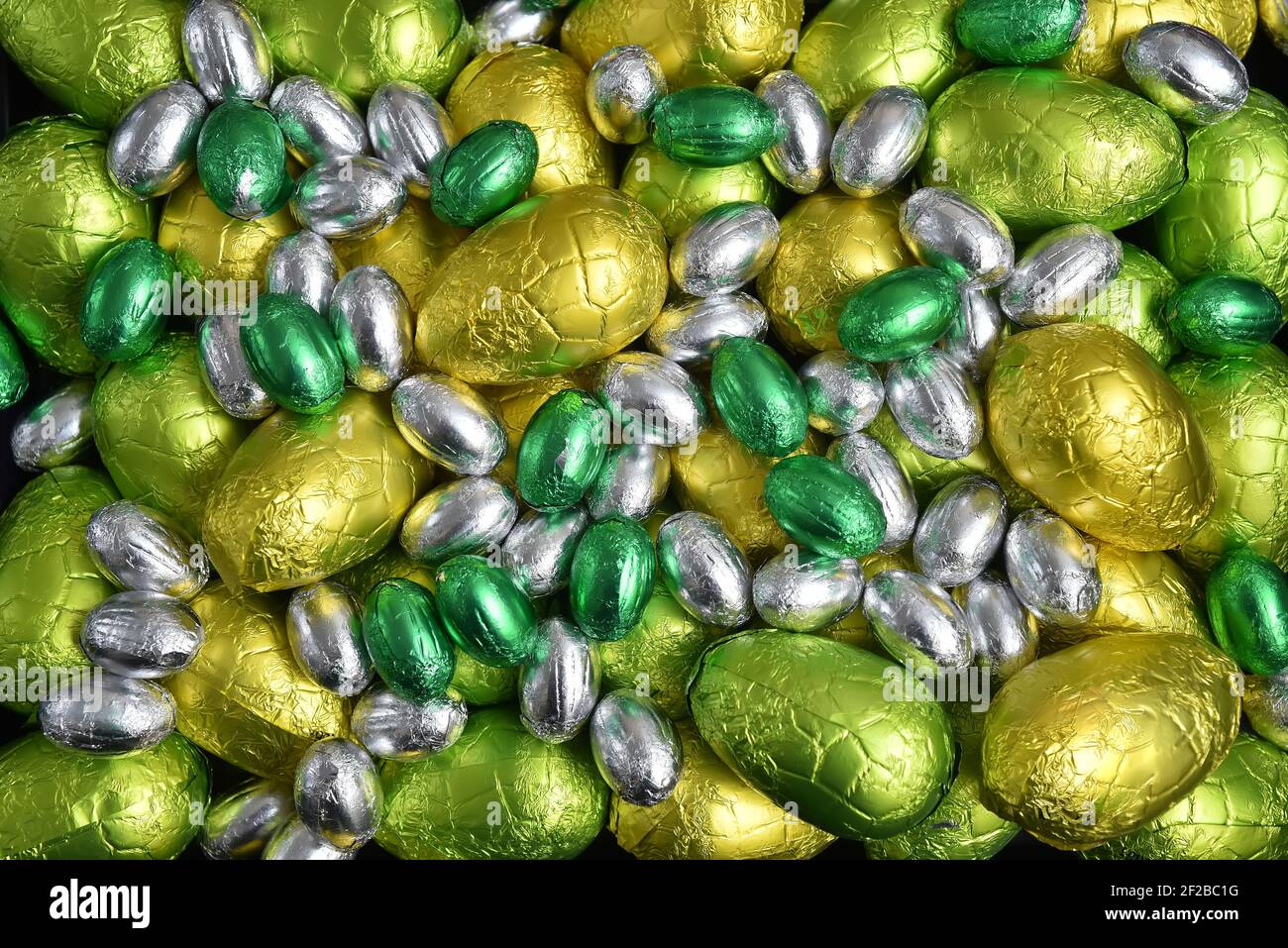 Große & kleine gelb, Gold, grün, lime grün und Silber Frühlingsfarben aus Folie umwickelten Schokolade ostereier, vor einem schwarzen Hintergrund. Stockfoto