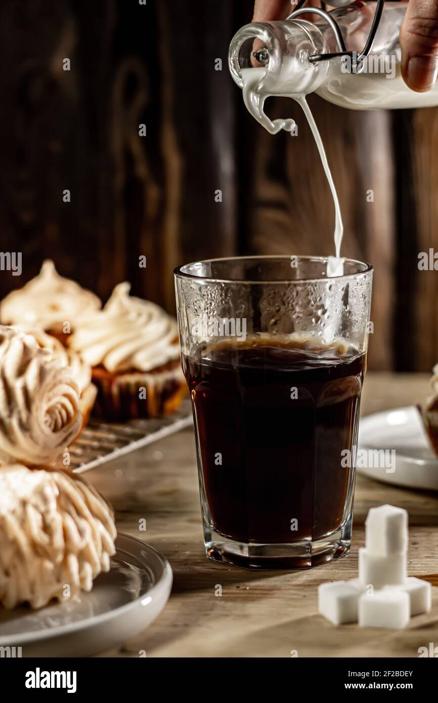Milch in ein Glas heißen Kaffee gießen. Stockfoto