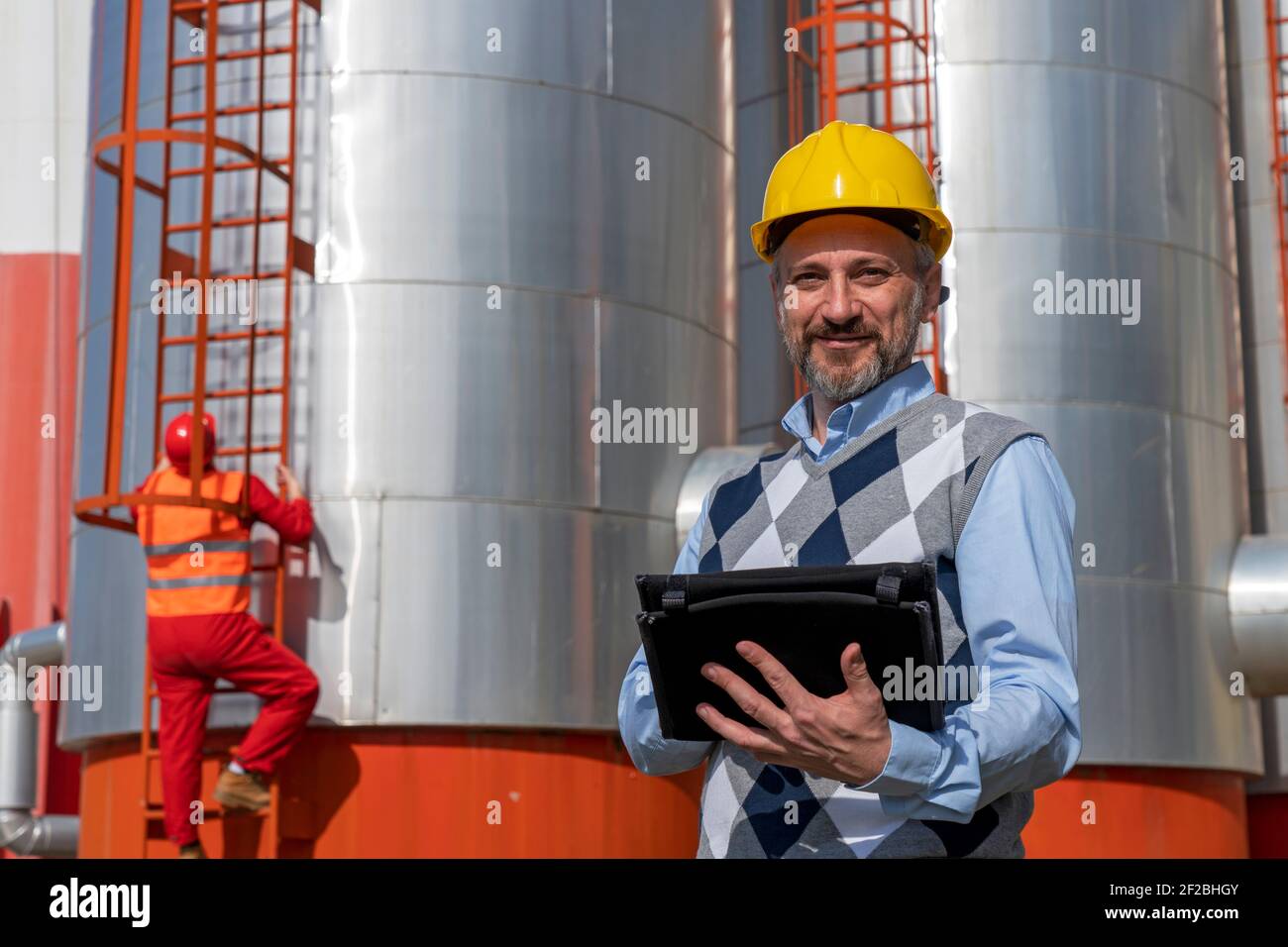 Portrait von businessperson in Gelbe Arbeit Helm mit digitalen Tablet in Ölraffinerie. Digitales Technologiekonzept. Industrie 4,0 Stockfoto