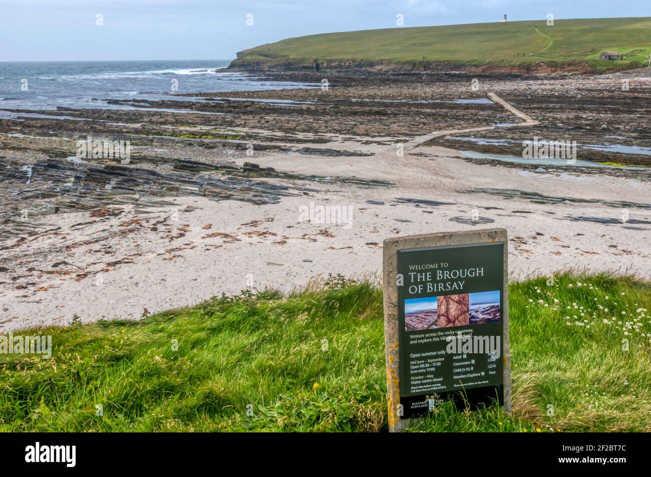 Historisches Schottland Willkommensschild nach Brough of Birsay, mit Damm zur Insel im Hintergrund. Stockfoto