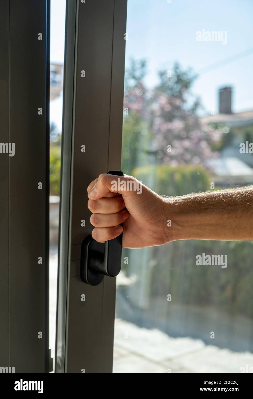 Männliches, von Hand geöffnetes Metall- oder PVC-Fenster, vertikale Nahaufnahme. Kippen und drehen graue Farbe Aluminium-Fenster, Mann hält den Griff, frische Luft für zu Hause. Stockfoto