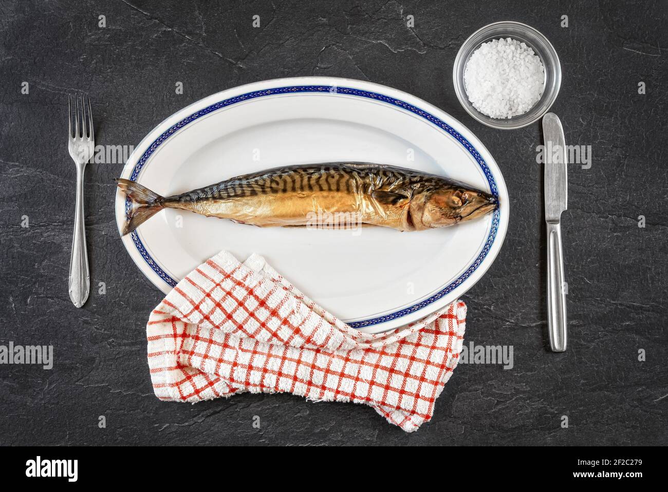 Ganze geräucherte Makrelenfische auf weißem ovalem Teller, grauschwarzer Stein wie Tischunterwand. Blick von oben Stockfoto