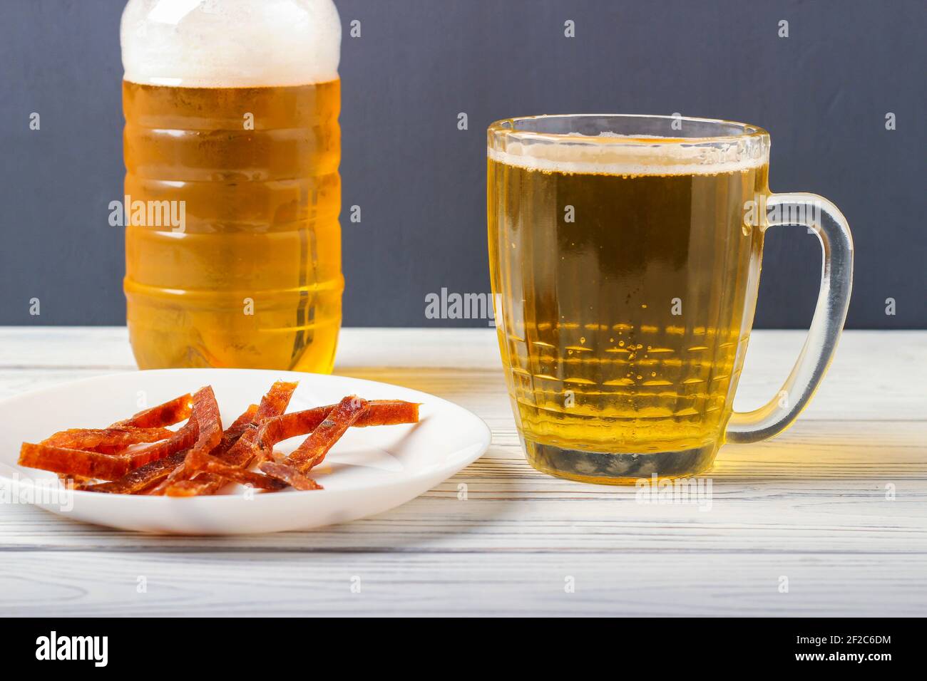 Bier in einem Becher auf dem Tisch und Scheiben Getrockneter gesalzener Fisch auf einer Platte Stockfoto