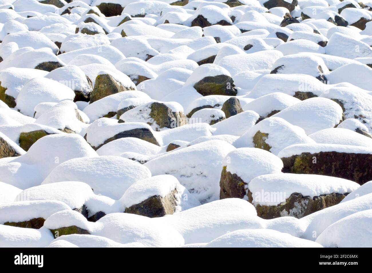 Felsbrocken, oder Felsrüstung, am Strand abgelagert, um Küstenerosion zu verhindern, wird durch eine Abdeckung von Neuschnee während eines besonders kalten Winters aufgeweicht Stockfoto