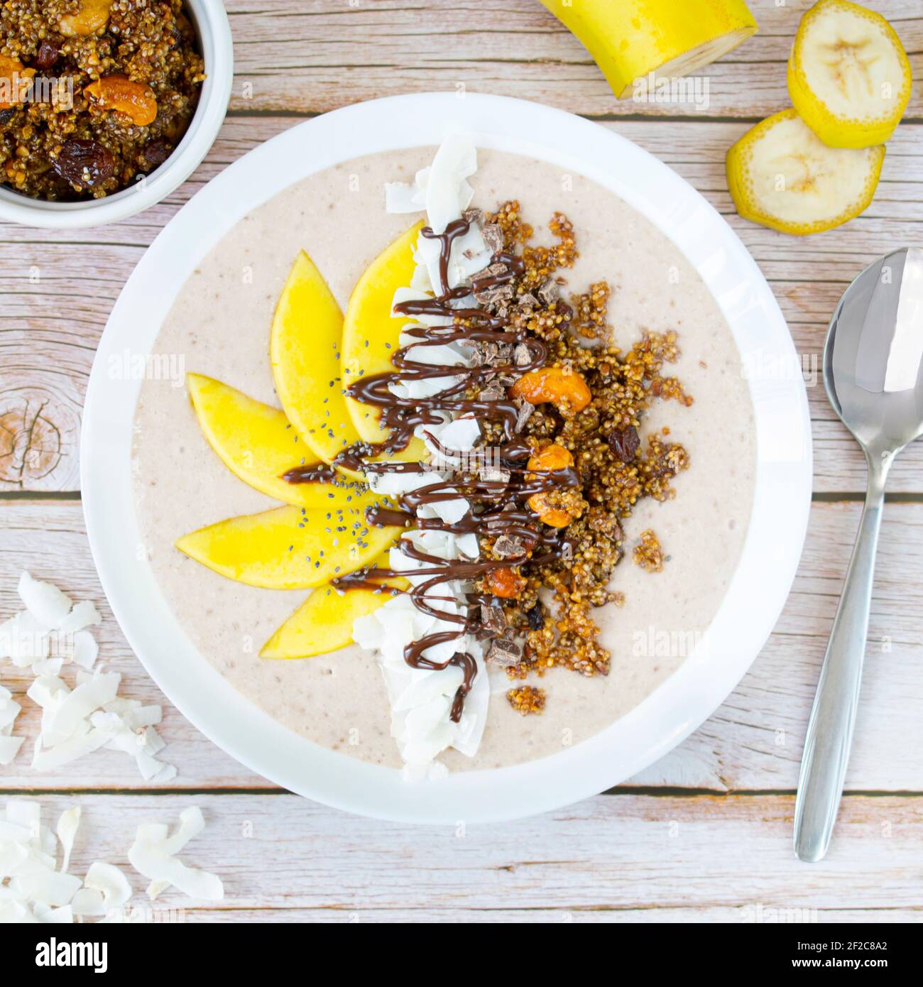 Schüssel Kokosnuss-Banane mit Quinoa-Granola und frischer Mangofrucht. Stockfoto