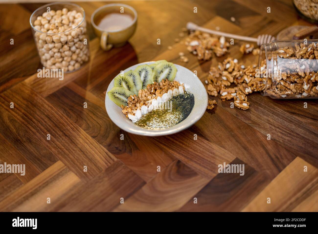 Gesundes Frühstück mit Müslischale mit Kiwi, Spirulina und Bio-Joghurt auf Holzplatte in der Küche mit Nüssen auf dem Hintergrund. Speicherplatz Kopieren. Stockfoto