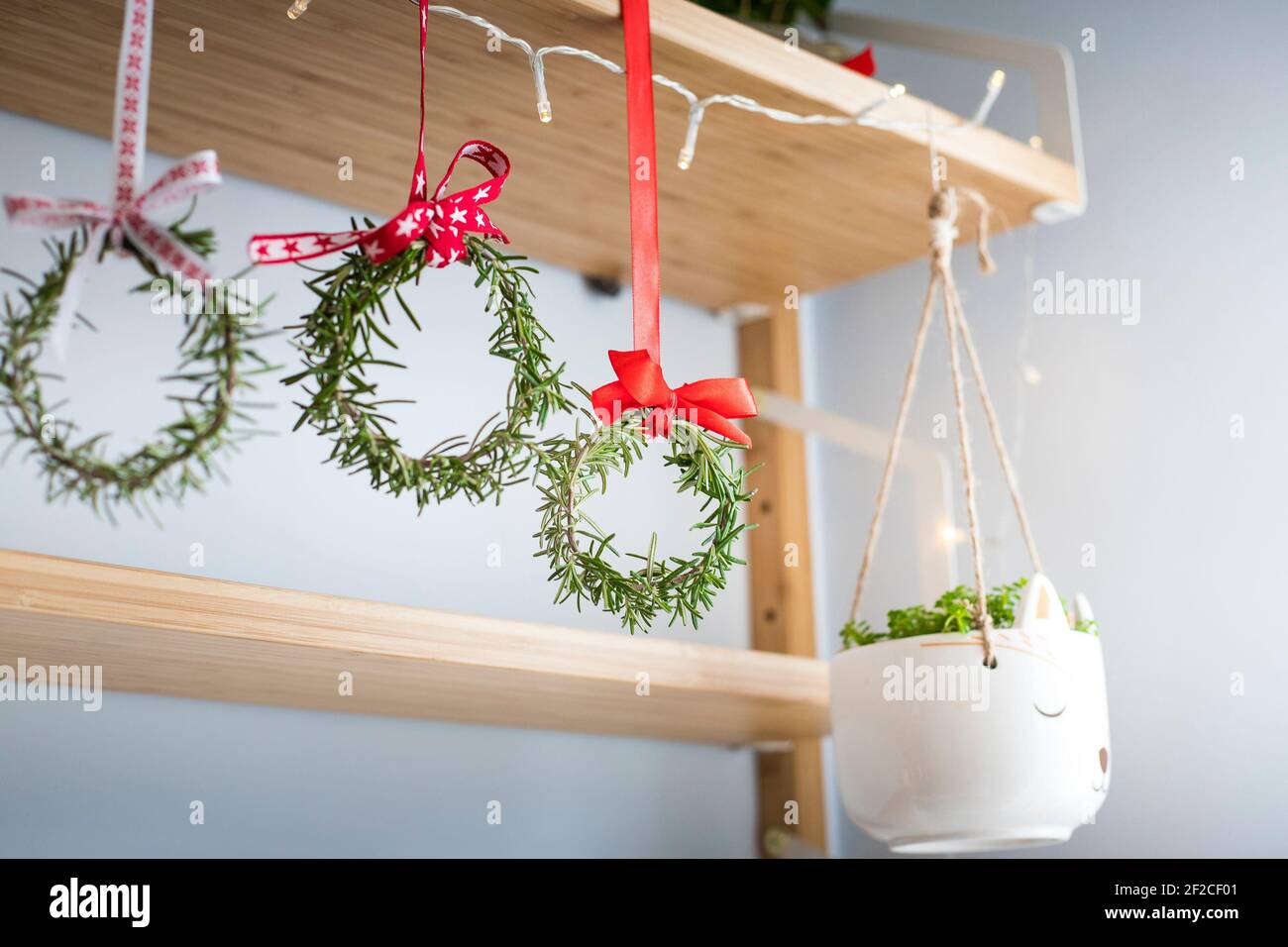 Drei Rosmarinkränze, die mit roten festlichen Bändern geschmückt sind und an einem Regal hängen. Natürliche Wohnkultur, diy, Idee für Weihnachten. Stockfoto