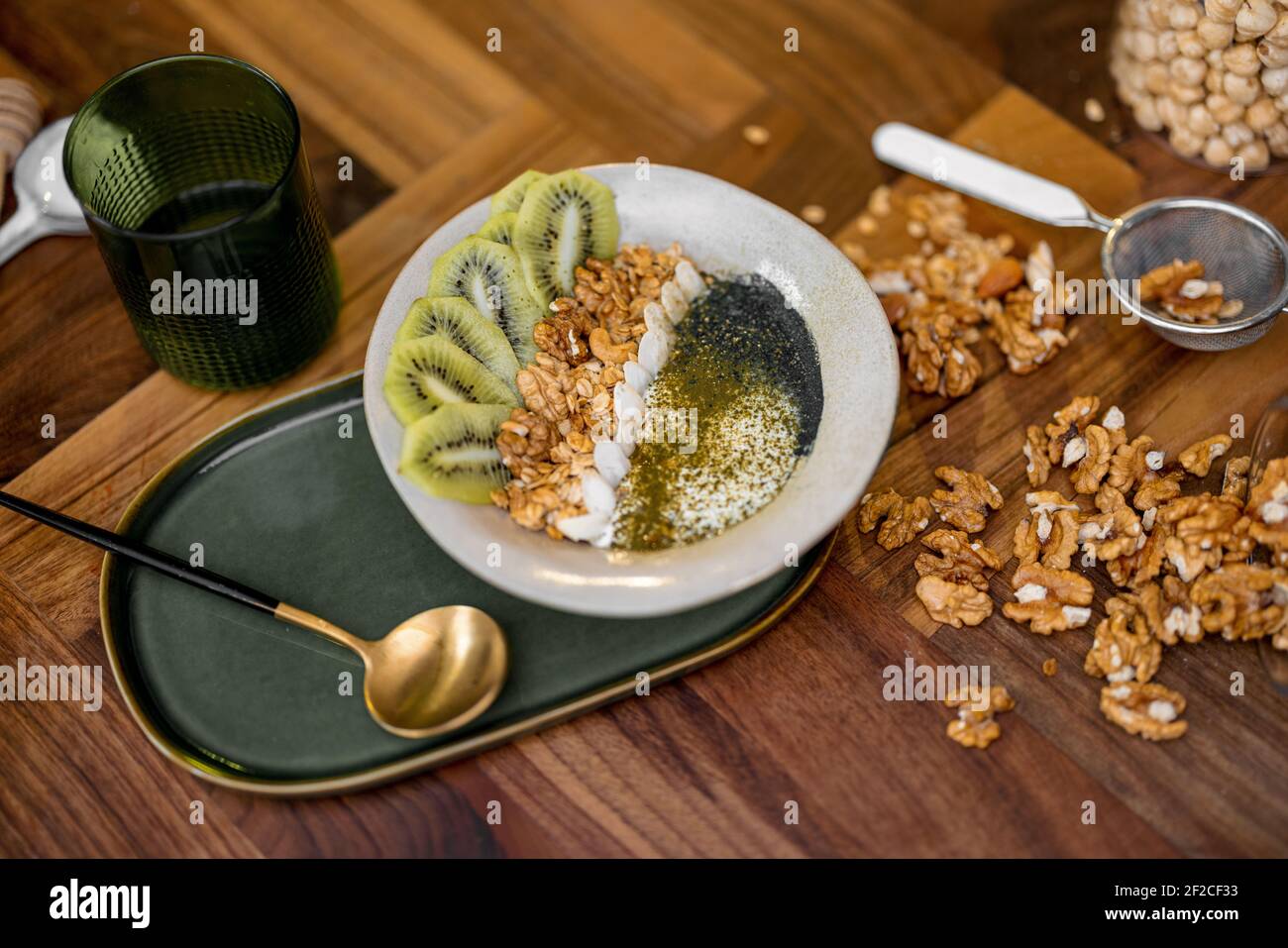 Gesundes Frühstück mit Müslischale mit Kiwi, Spirulina und Bio-Joghurt auf Holzplatte in der Küche mit Nüssen auf dem Hintergrund. Stockfoto
