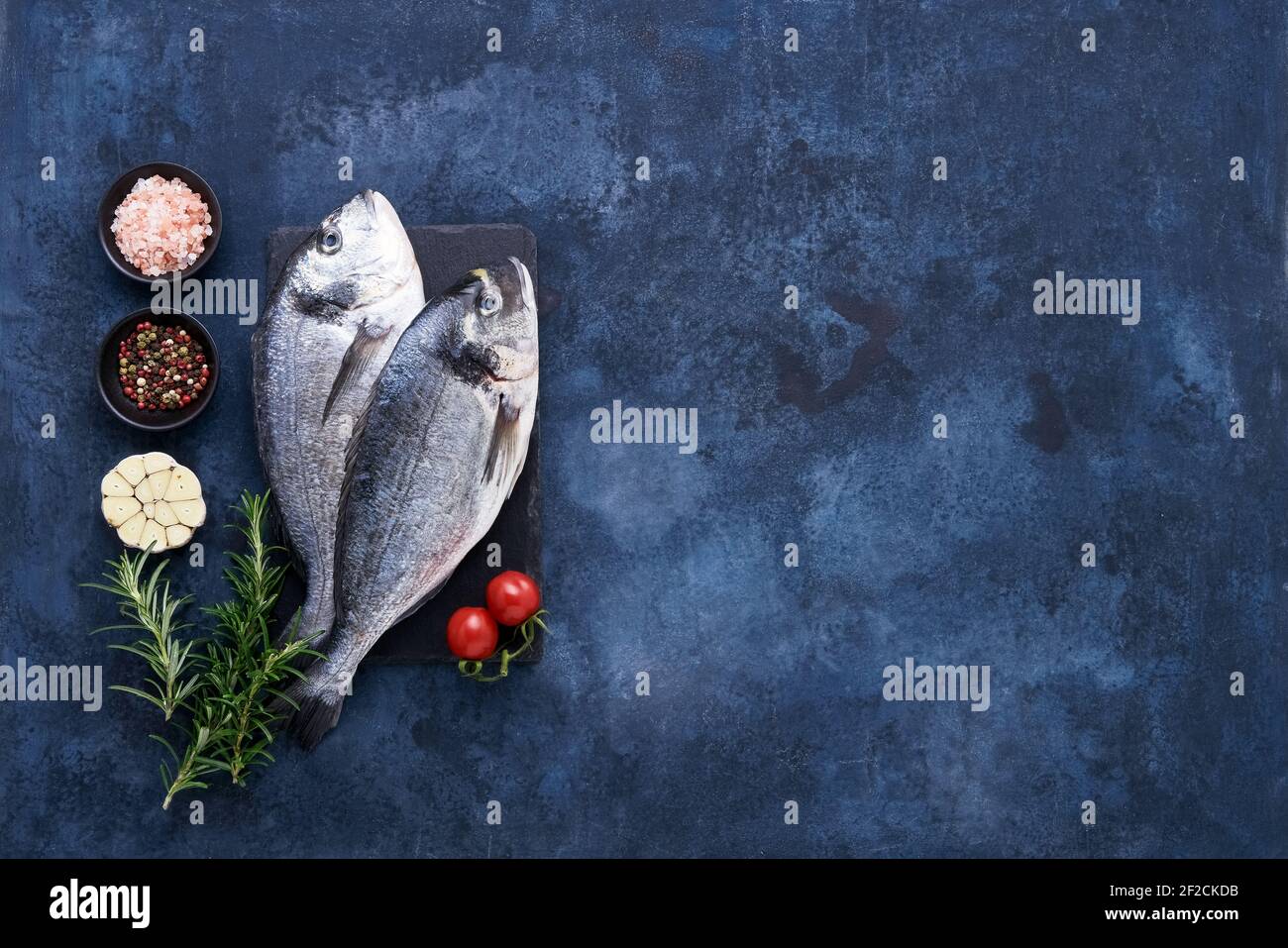 Roher dorado-Fisch mit Gewürzen auf einem Schieferschneidebrett auf blauem Hintergrund. Mediterranes Meeresfrüchtekonzept. Draufsicht, Kopierbereich für Text Stockfoto