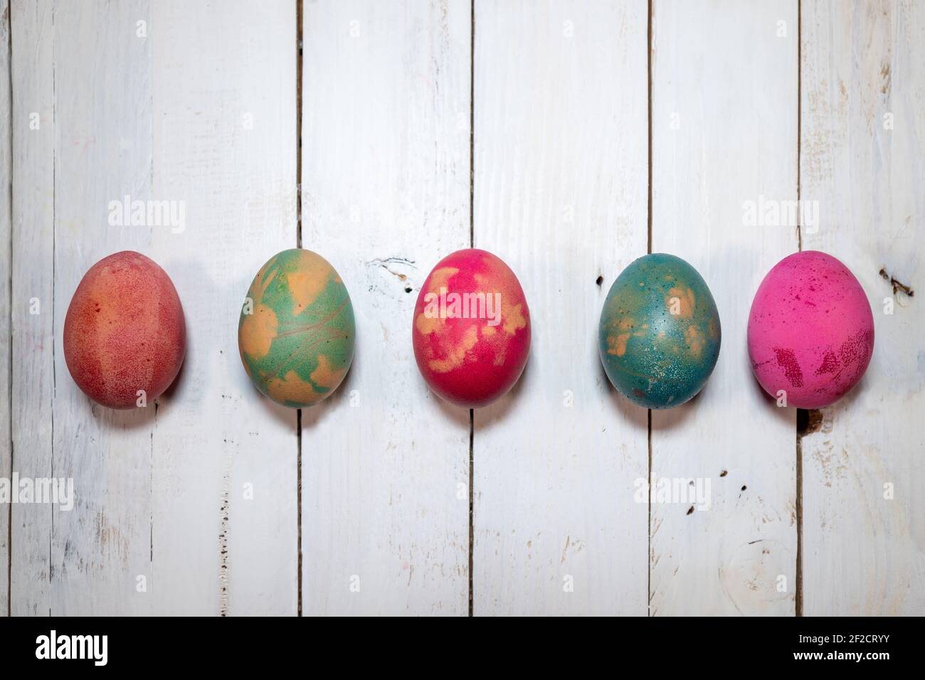 Eine hausgemachte natürliche Art, Ostereier zu dekorieren. Fünf gekochte Eier mit Farben, Blättern und Blumen auf einem schäbigen schicken Holztisch bemalt. Stockfoto