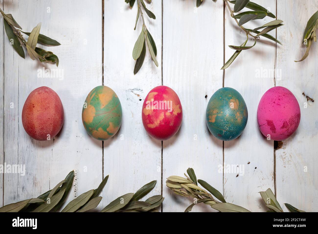 Zwei Ostersymbole: Eier und Olivenzweige. Fünf farbige Eier mit Olivenzweigen um sie herum auf einem schäbigen schicken Holztisch. Stockfoto