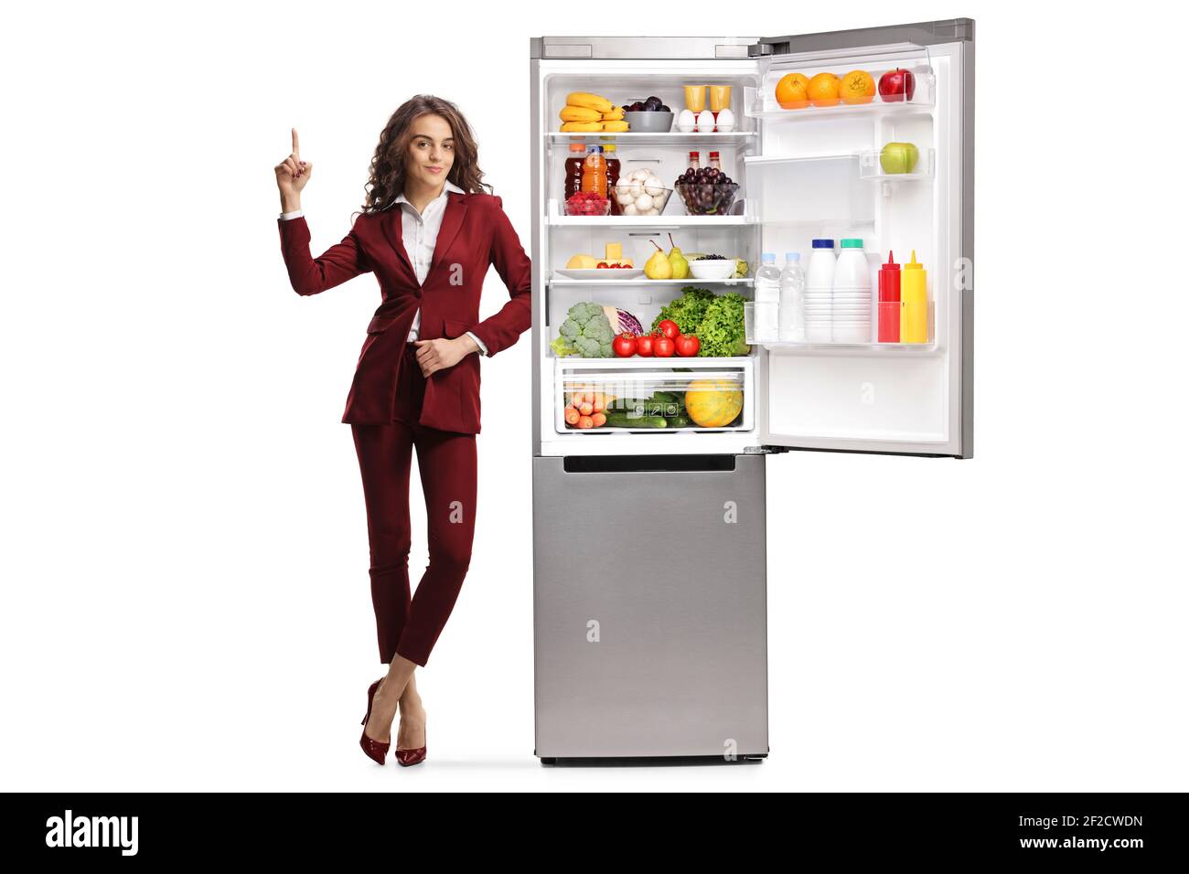 Ganzkörperportrait einer jungen Frau, die sich auf eine lehnt Öffnen Sie den Kühlschrank und zeigen Sie isoliert auf weißem Hintergrund Stockfoto