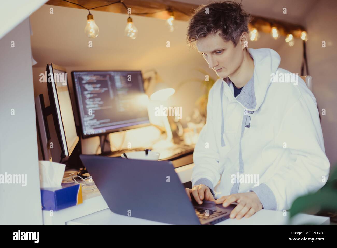 Ein Mann, der an einem Schreibtisch sitzt und von zu Hause aus an seinem Computer arbeitet. IT-Spezialist Programmierer schreiben Code auf seinem pc und Laptop. Entwickler Remote Home Office. F Stockfoto