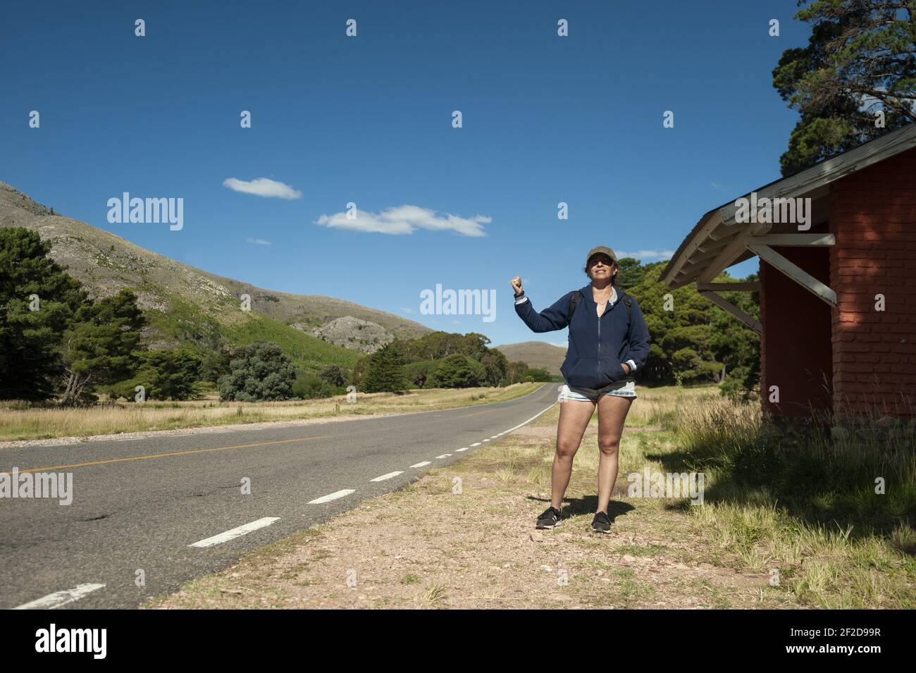 Eine Argentinierin mittleren Alters, die glücklich auf der Bergstraße trampiert Stockfoto