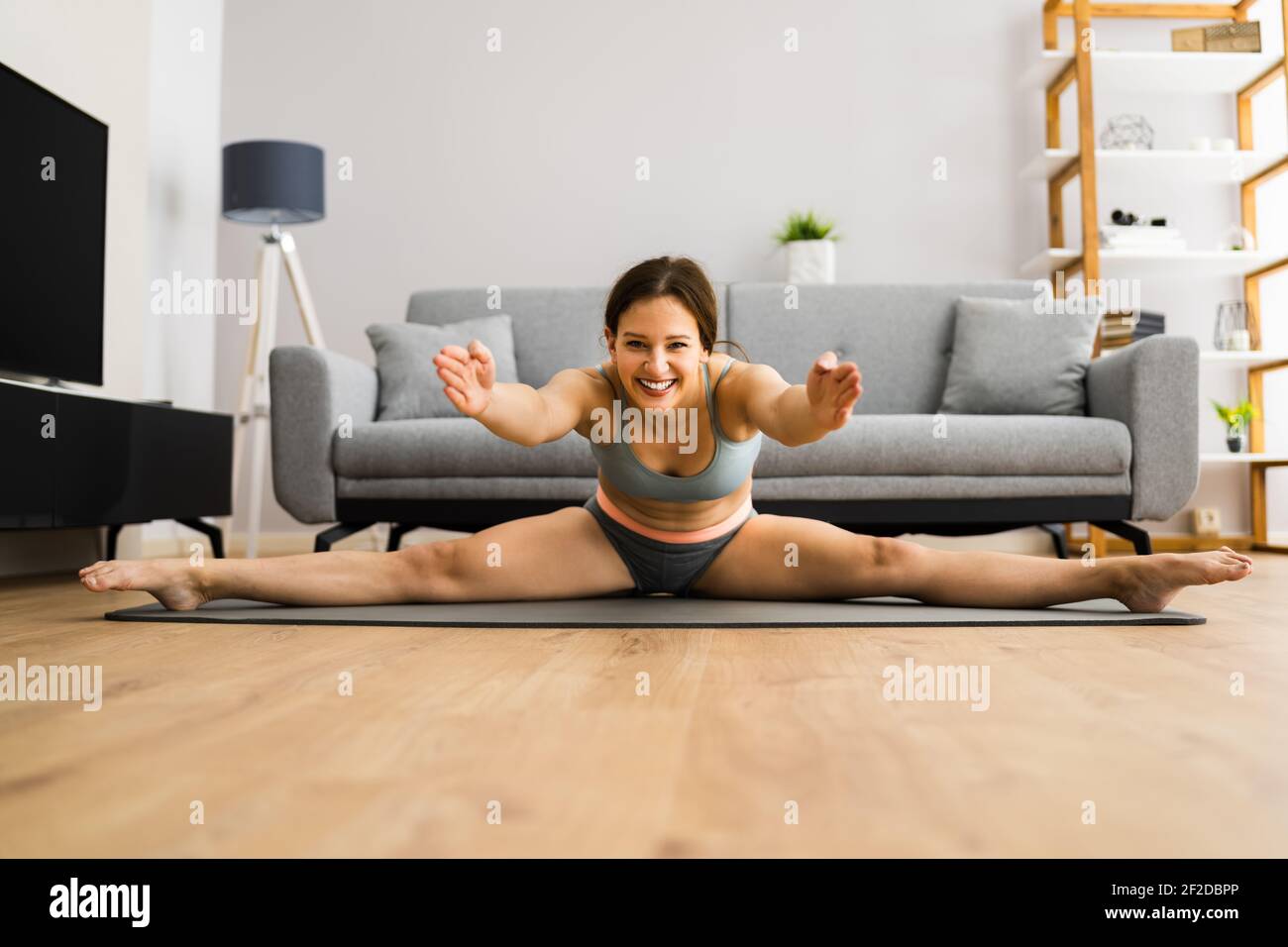 Junge Frau In Split Stretching Sport Pose Zu Hause Stockfoto