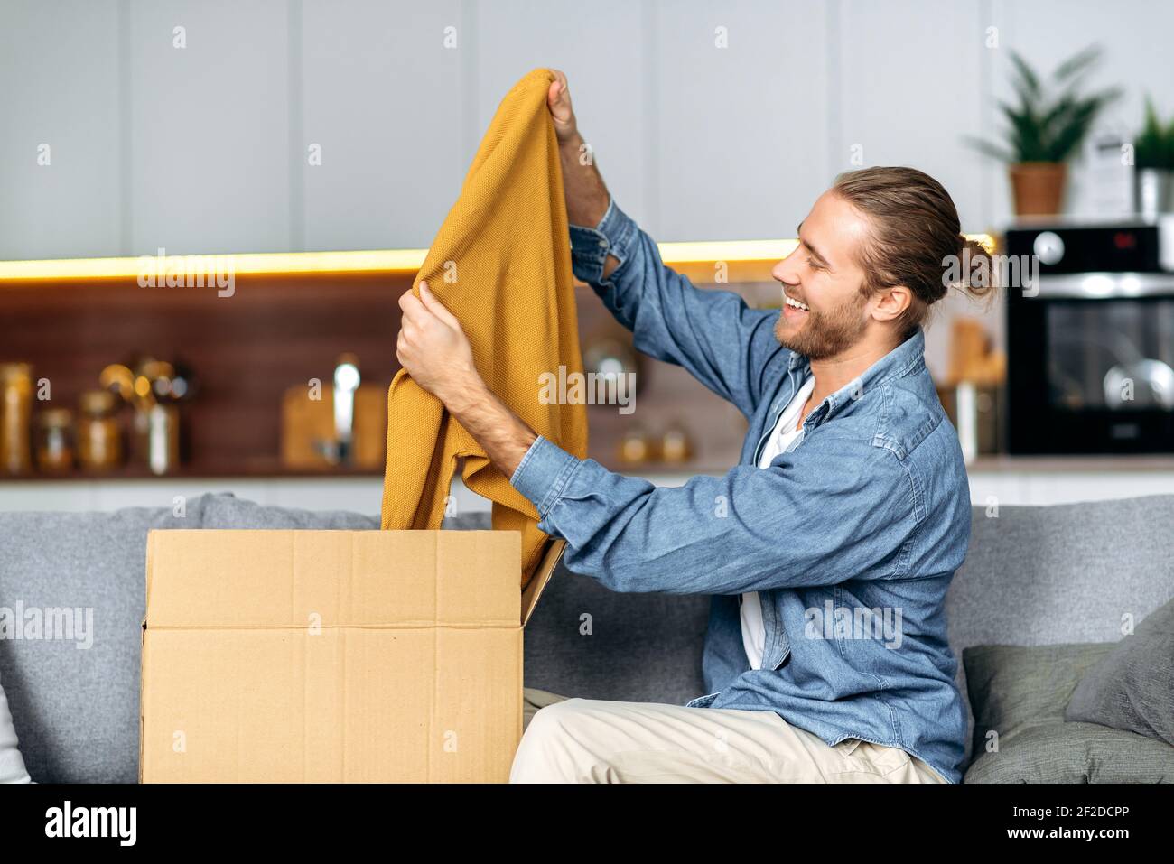 Lächelnder attraktiver Mann packte sein Paket aus und freute sich, eine  lange erwartete Bestellung zu bekommen. Kaukasischen modernen Kerl  Einkaufen in Internet-Shops, Kauf neuer Kleidung online,  Online-Shopping-Konzept Stockfotografie - Alamy