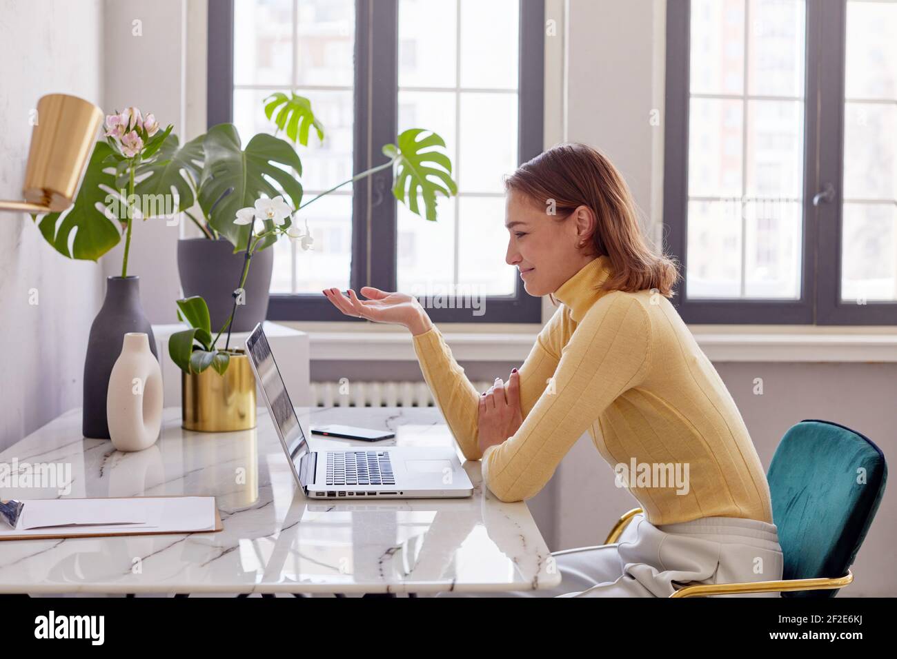 Seitenansicht der Frau in smart casual Outfit gestikulierend und Sprechen während eines Online-Meetings in einem kreativen Arbeitsbereich Stockfoto