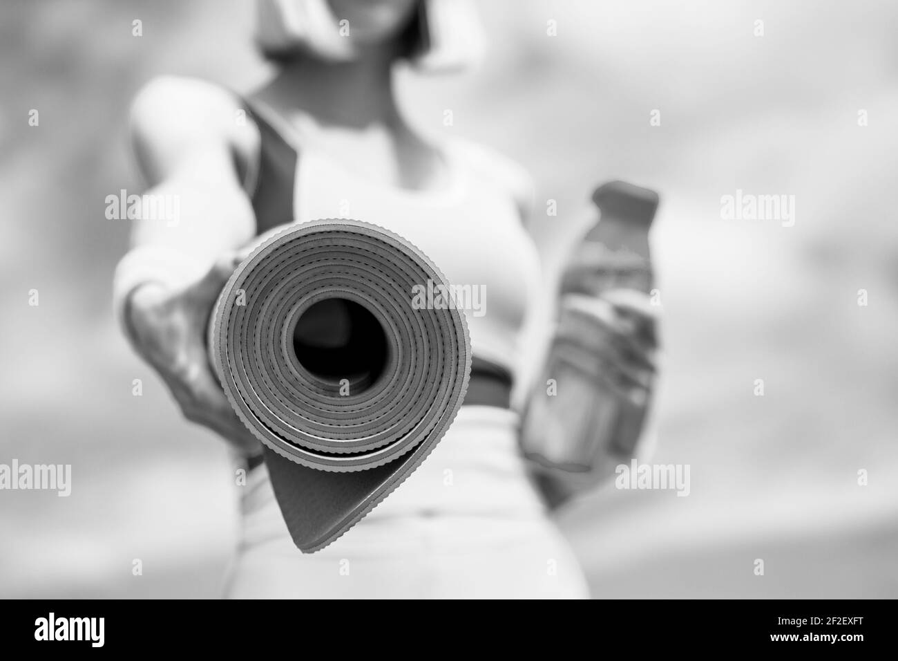 Fitness-Mädchen mit Yoga-Matte über Himmel Hintergrund. Frau in Sportkleidung hält eine Yogamatte und eine Flasche Wasser. Yogamatte und Wasserflasche. Nahaufnahme Stockfoto