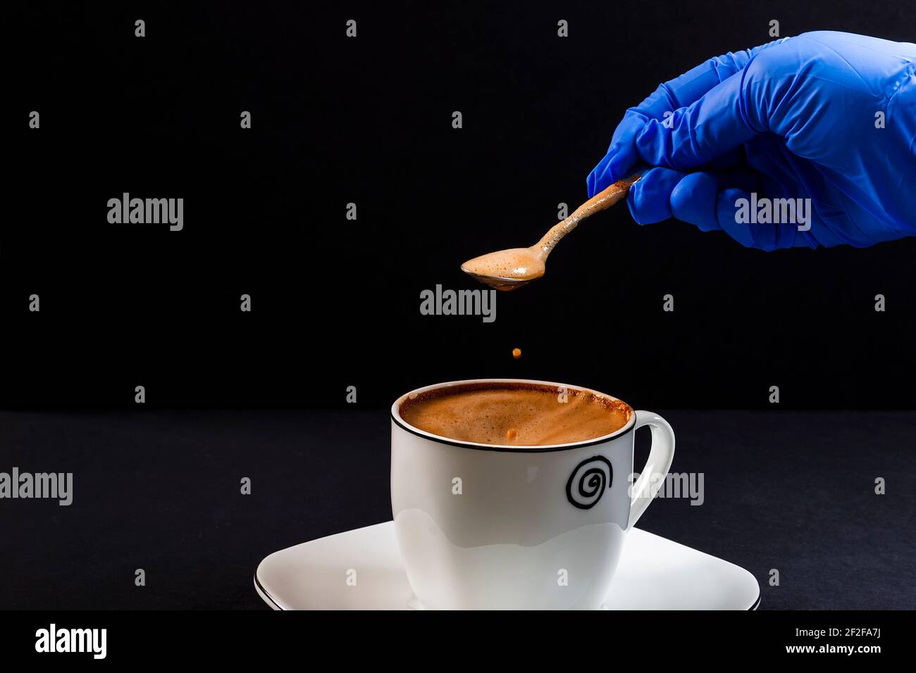 Tropfen Kaffee mit Milch, die aus einem Löffel fällt Von der Hand einer Person mit Latex gehalten Handschuh.Dies ist ein horizontales Format Foto auf schwarzer Rückseite aufgenommen Stockfoto