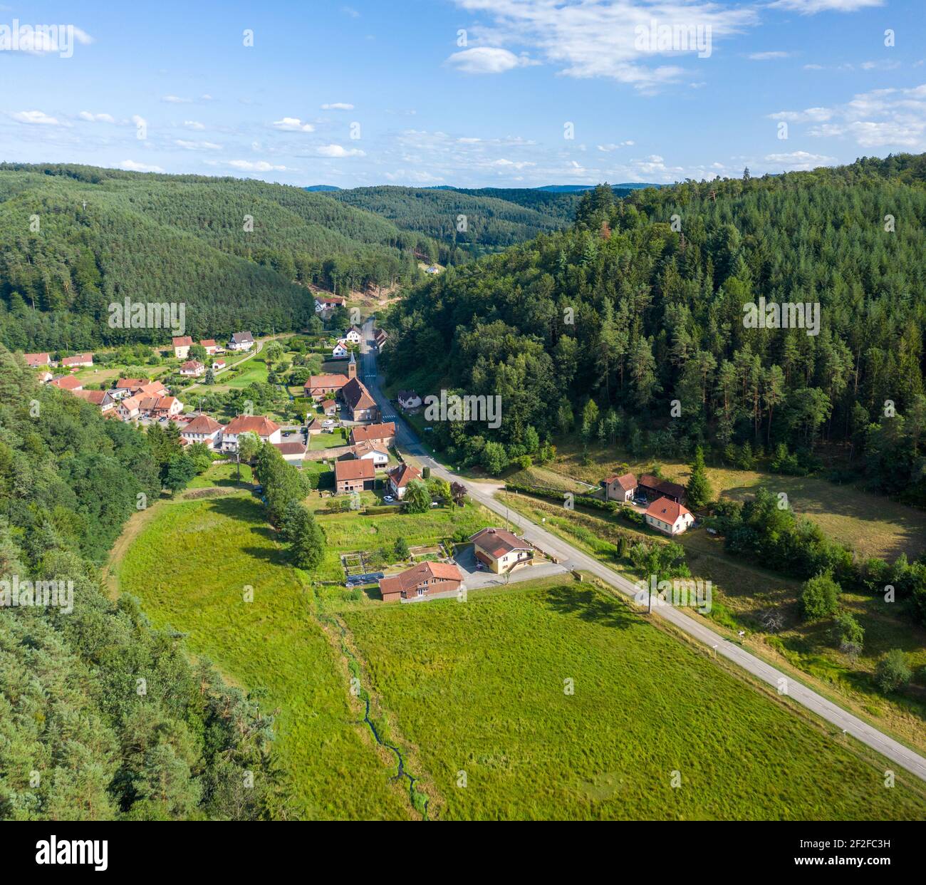 Drohne Blick auf Bergdorf. Mehrere Häuser und Kirche entlang der Straße zwischen Wäldern. Sturzelbronn, Moselle, Frankreich. Stockfoto