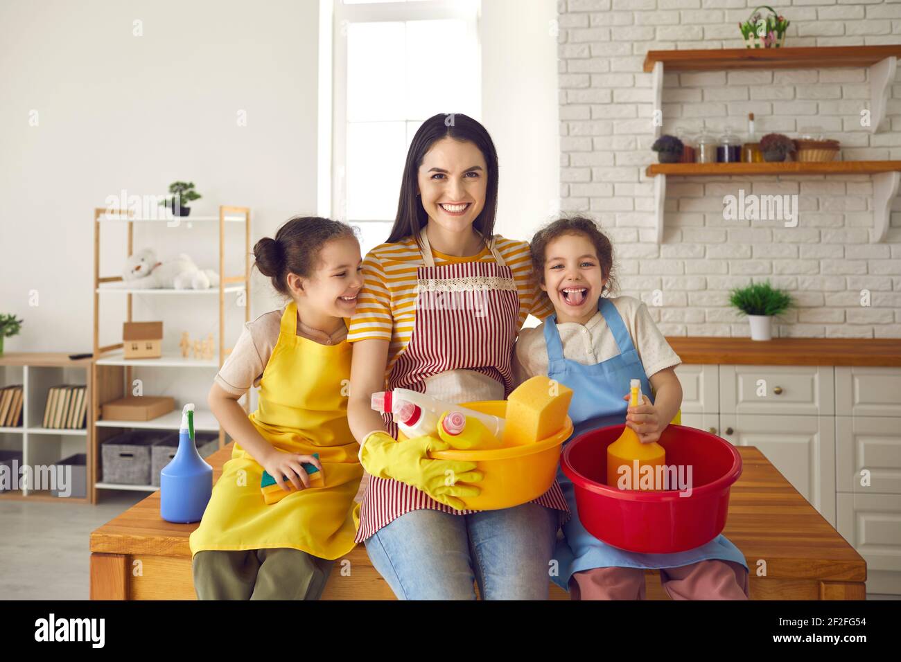 Mutter mit Töchtern mit Reinigungsmitteln in den Händen, die bereit sind, das Haus aufzuräumen. Stockfoto