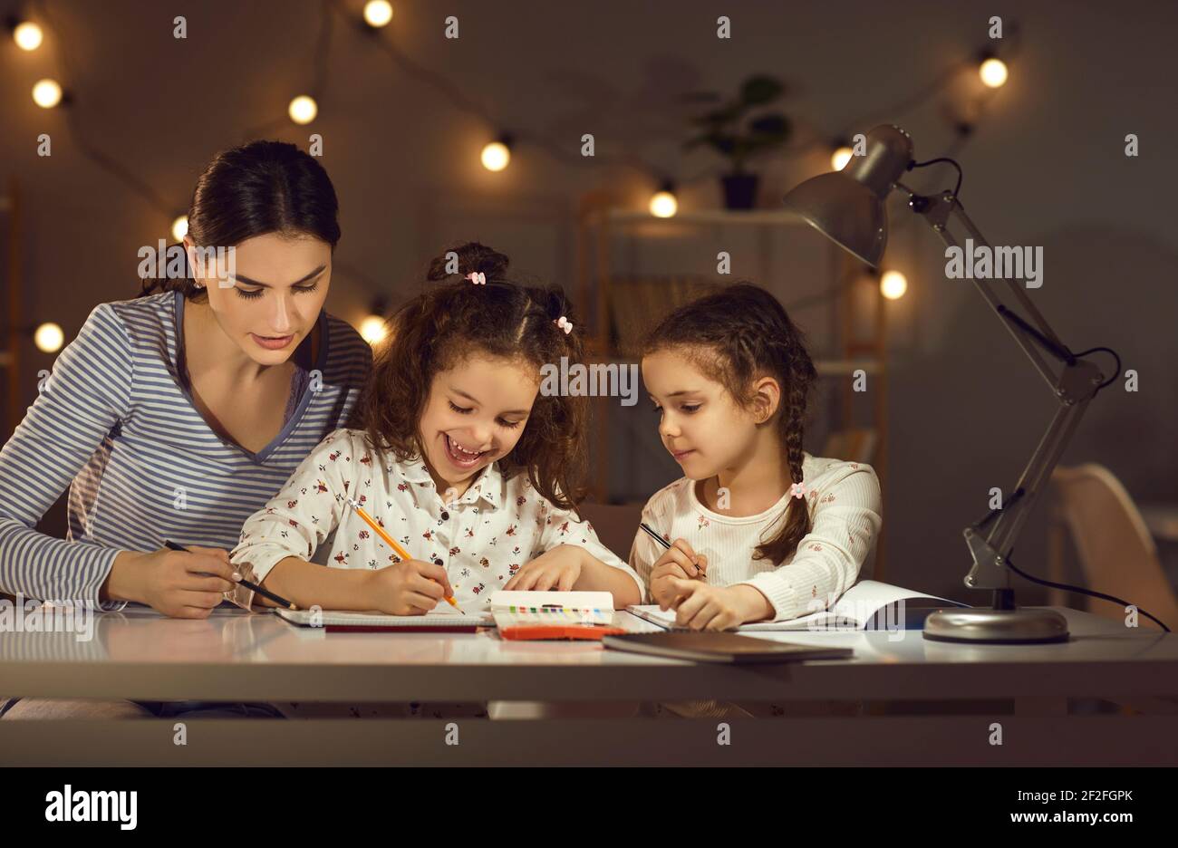 Mutter mit Töchtern, die auf Papier zeichnen und Hausaufgaben zu Hause machen Abends Stockfoto