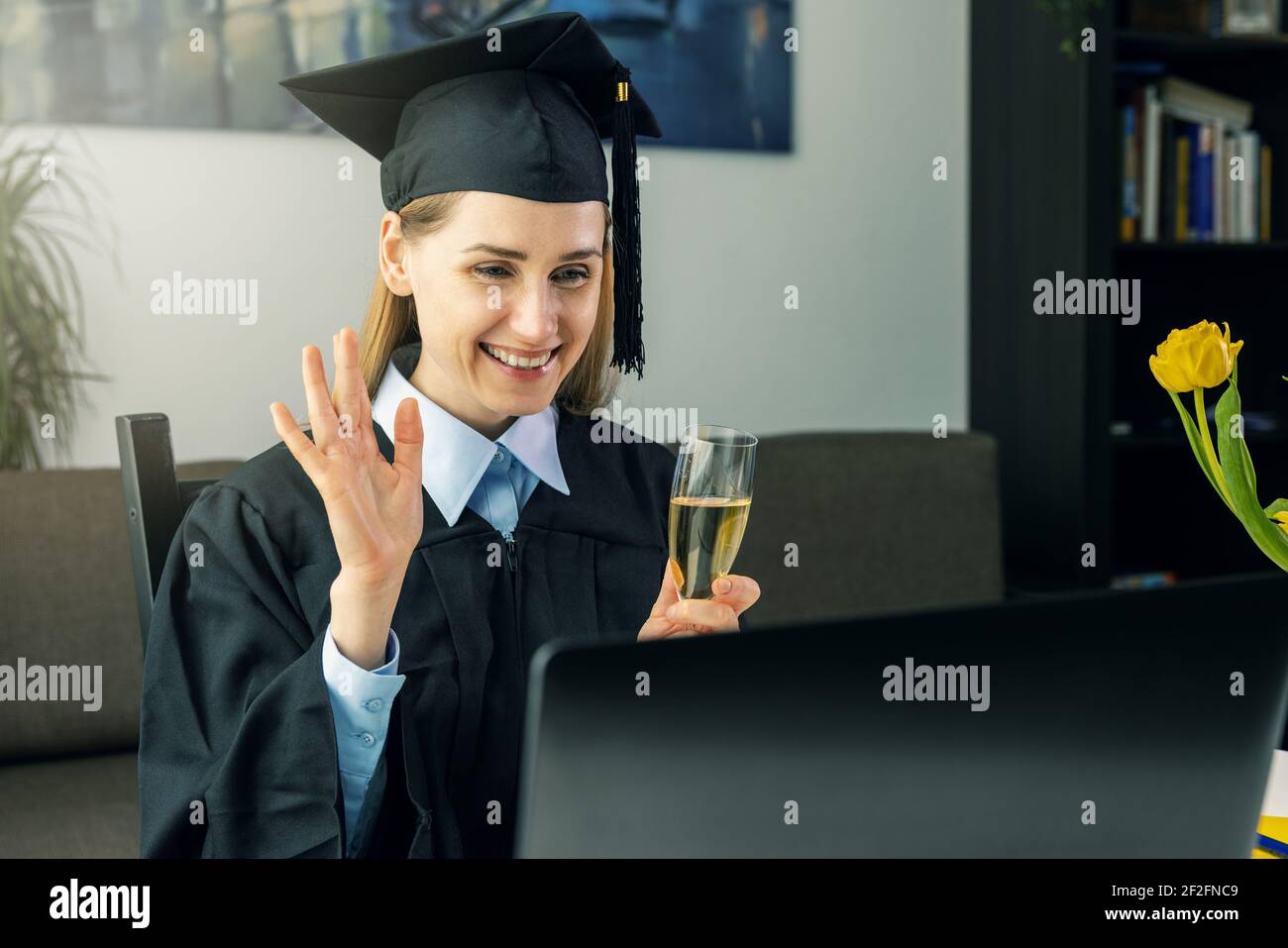 Soziale Distanzierung Graduierung Partei - weibliche Absolvent trägt Kleid und Feiern Sie Bachelor-Abschluss online mit College-Freunden zu Hause Stockfoto
