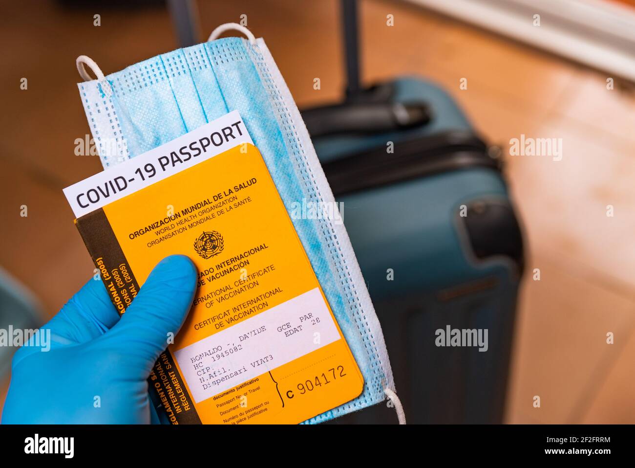 Hand mit Latex-Handschuhe halten covid Impfstoff Pass und Gesichtsmaske Konzept mit Gepäck am Flughafen. Reisen und Tourismus während covid19 Pandemie wit Stockfoto